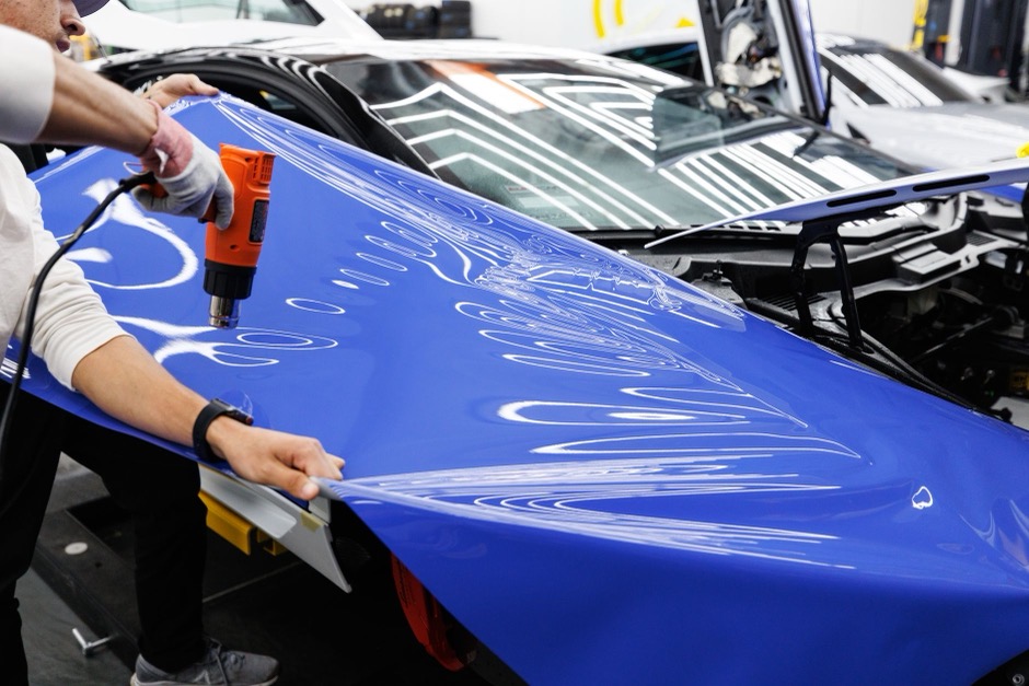 A technician using a heat gun to apply a blue vinyl wrap to a car