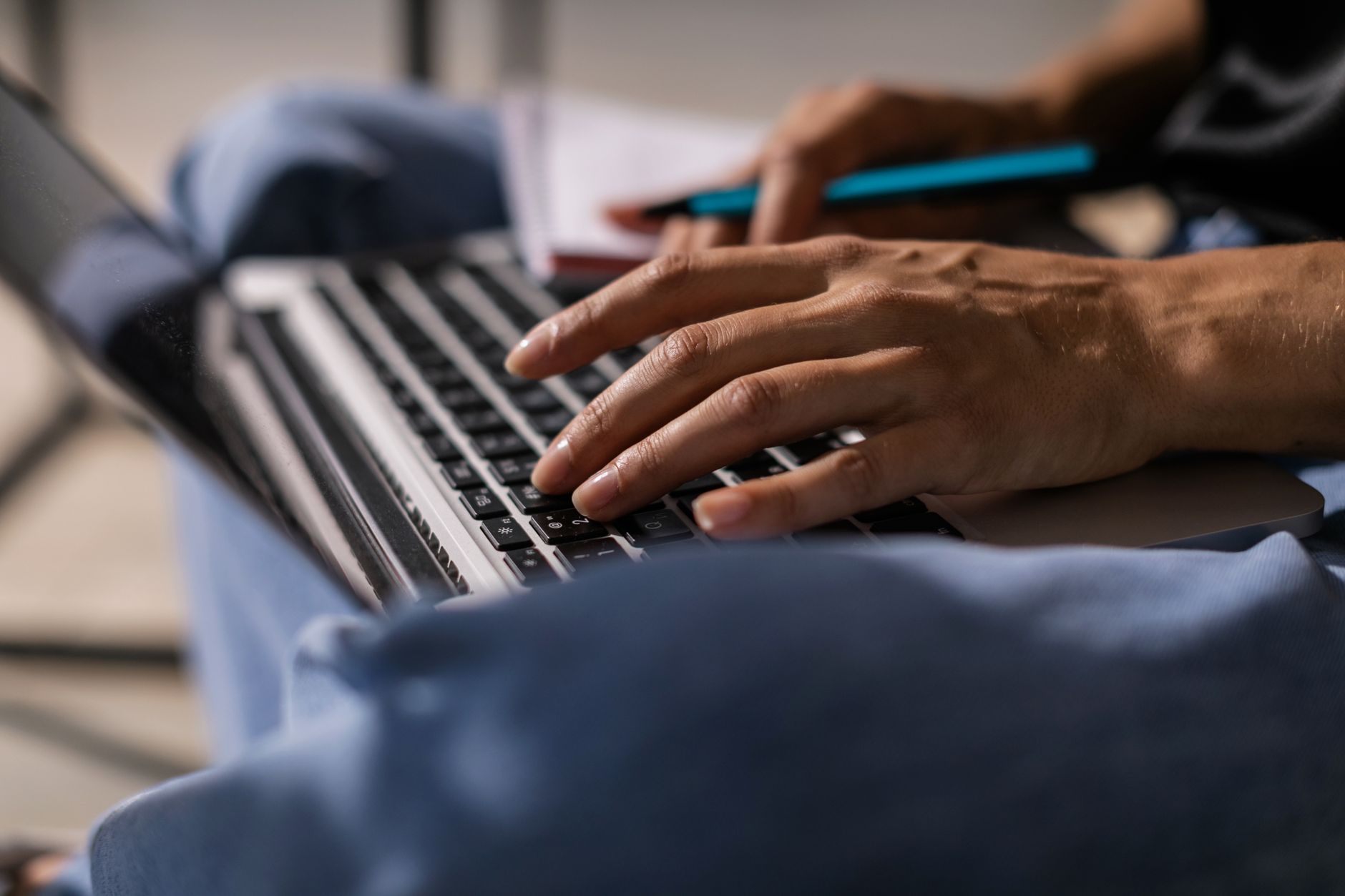 A person typing on a laptop with notes and a coffee nearby