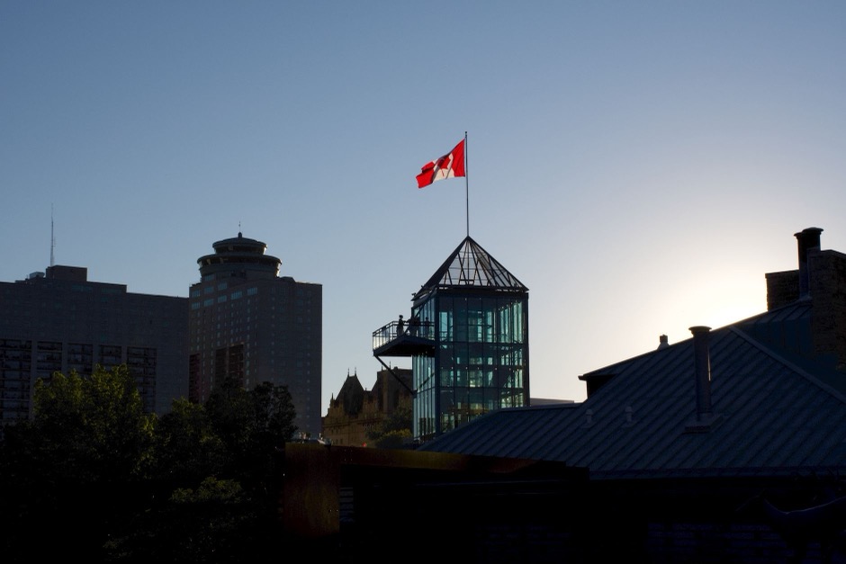 Winnipeg skyline silhouetted against a sunset sky with a Canadian flag